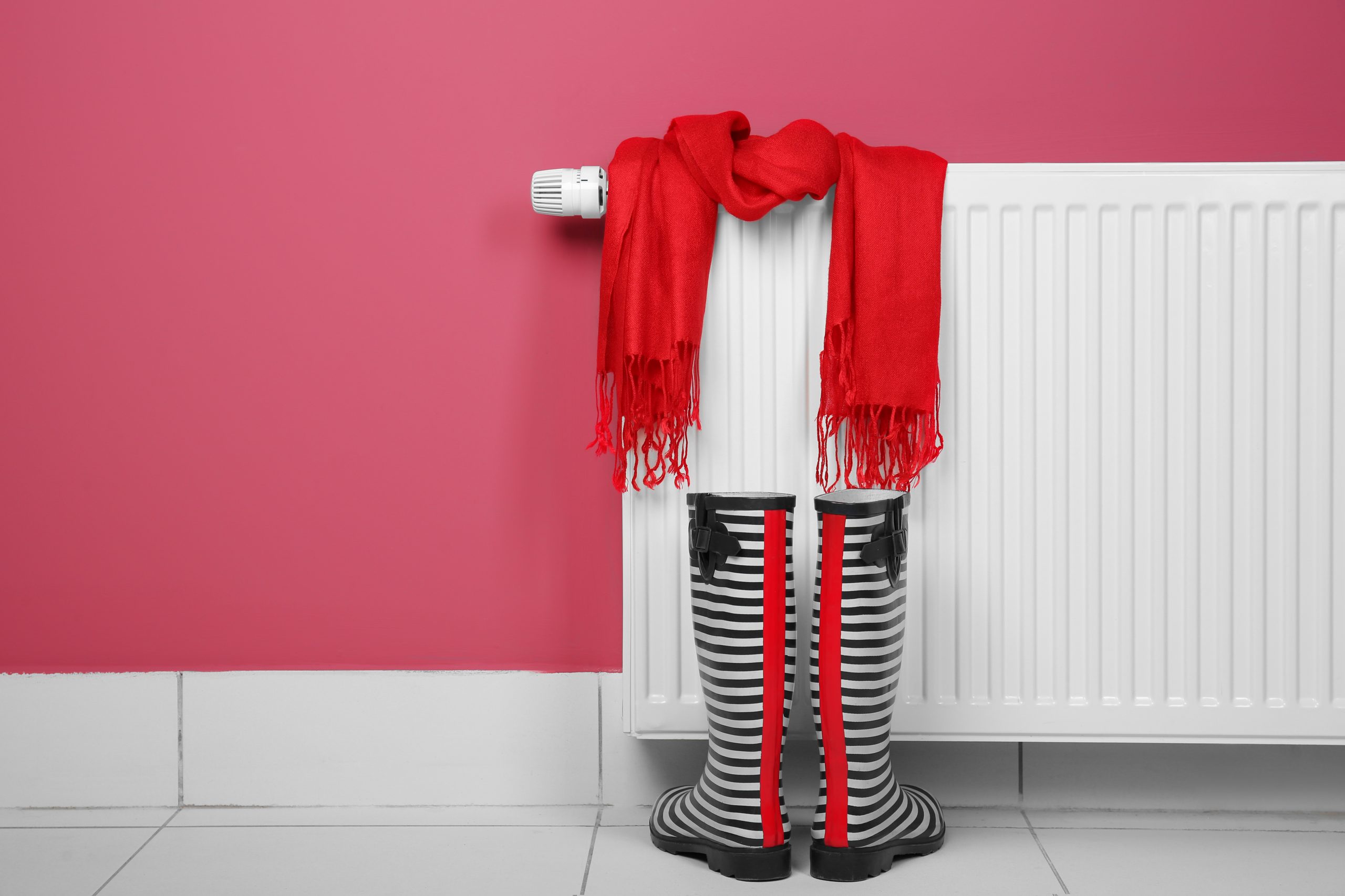 Gumboots and scarf near heating radiator on pink background